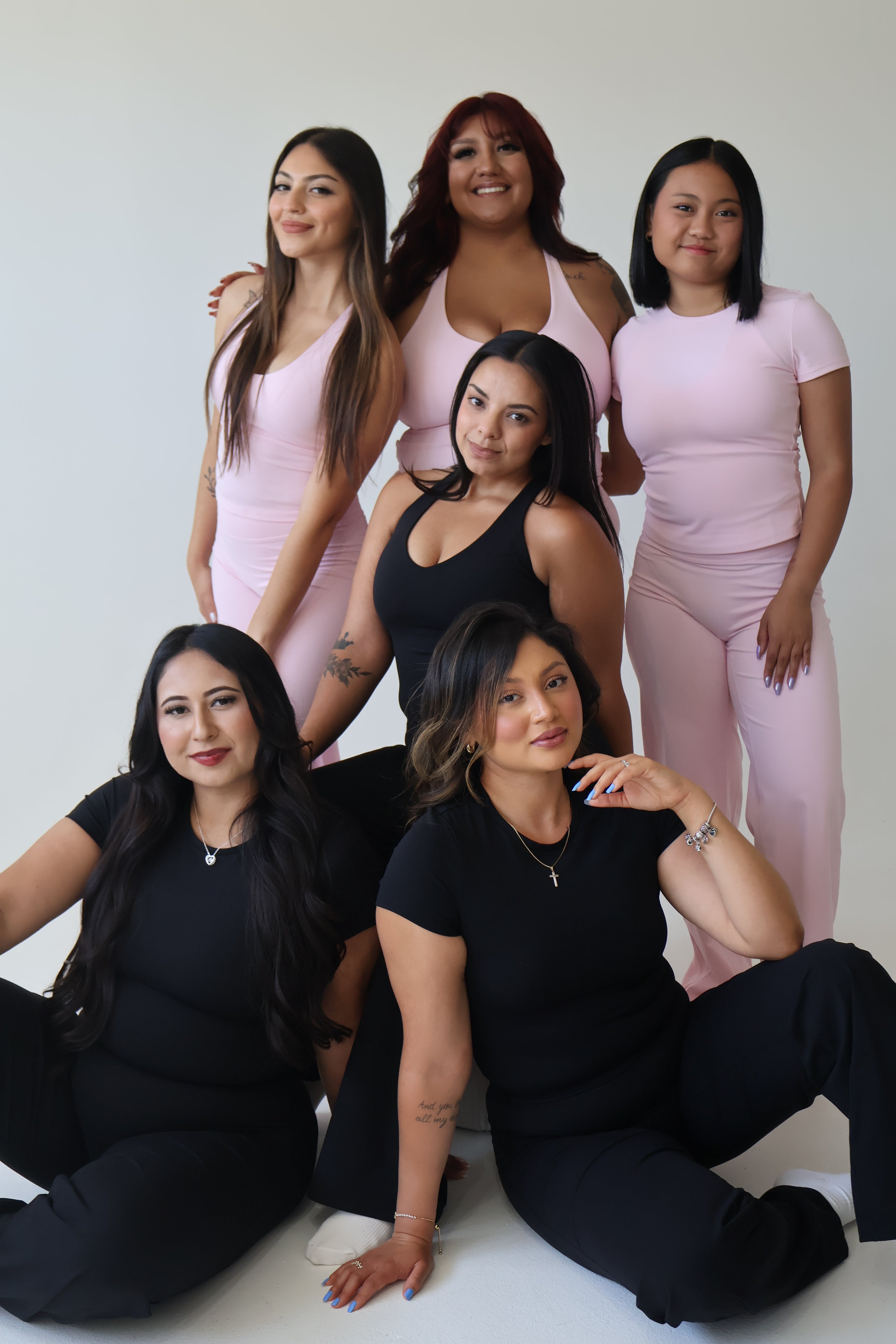 Six women wearing WAVE Motion activewear in blush pink and black, showcasing racerback tanks and straight-leg pants in a studio group portrait.